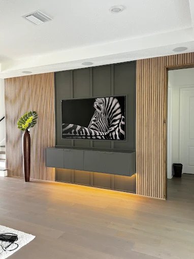 Wood slat media wall with a wall-mounted television, floating console and warm under-cabinet lighting.