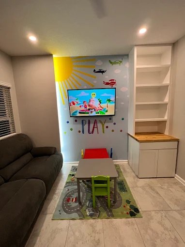 Children's room with a wall-mounted television, built-in white shelving and cabinetry.